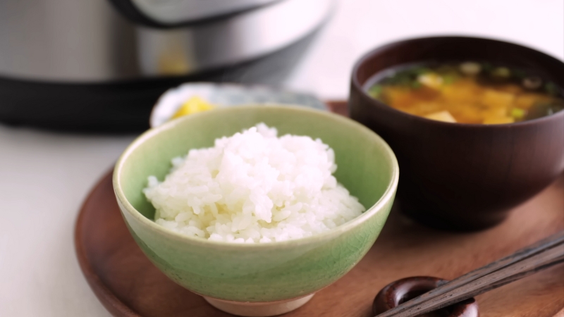 A small bowl of leftover sushi rice is served on a wooden tray next to miso soup and chopsticks