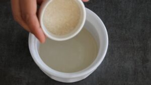 Sugar is being added to a bowl of rice vinegar to prepare sushi seasoning