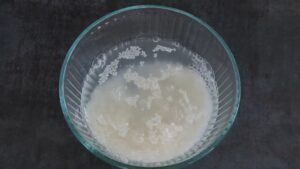 Short-grain sushi rice is being rinsed in a glass bowl filled with cloudy water to remove excess starch
