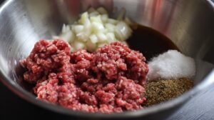 Ground beef with chopped onions and seasonings in a mixing bowl