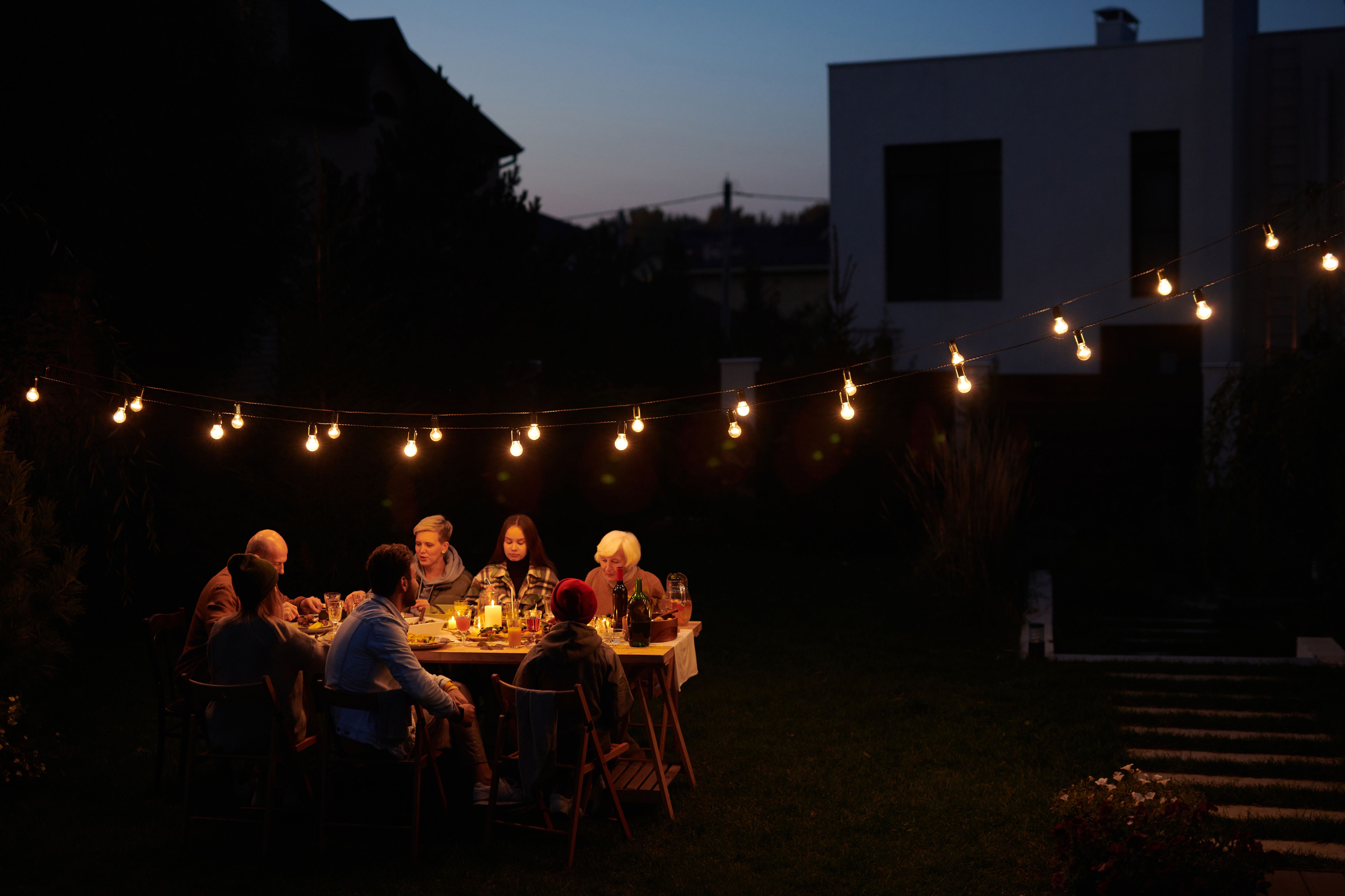 A family enjoying an evening meal outdoors under decorative string lights in a garden