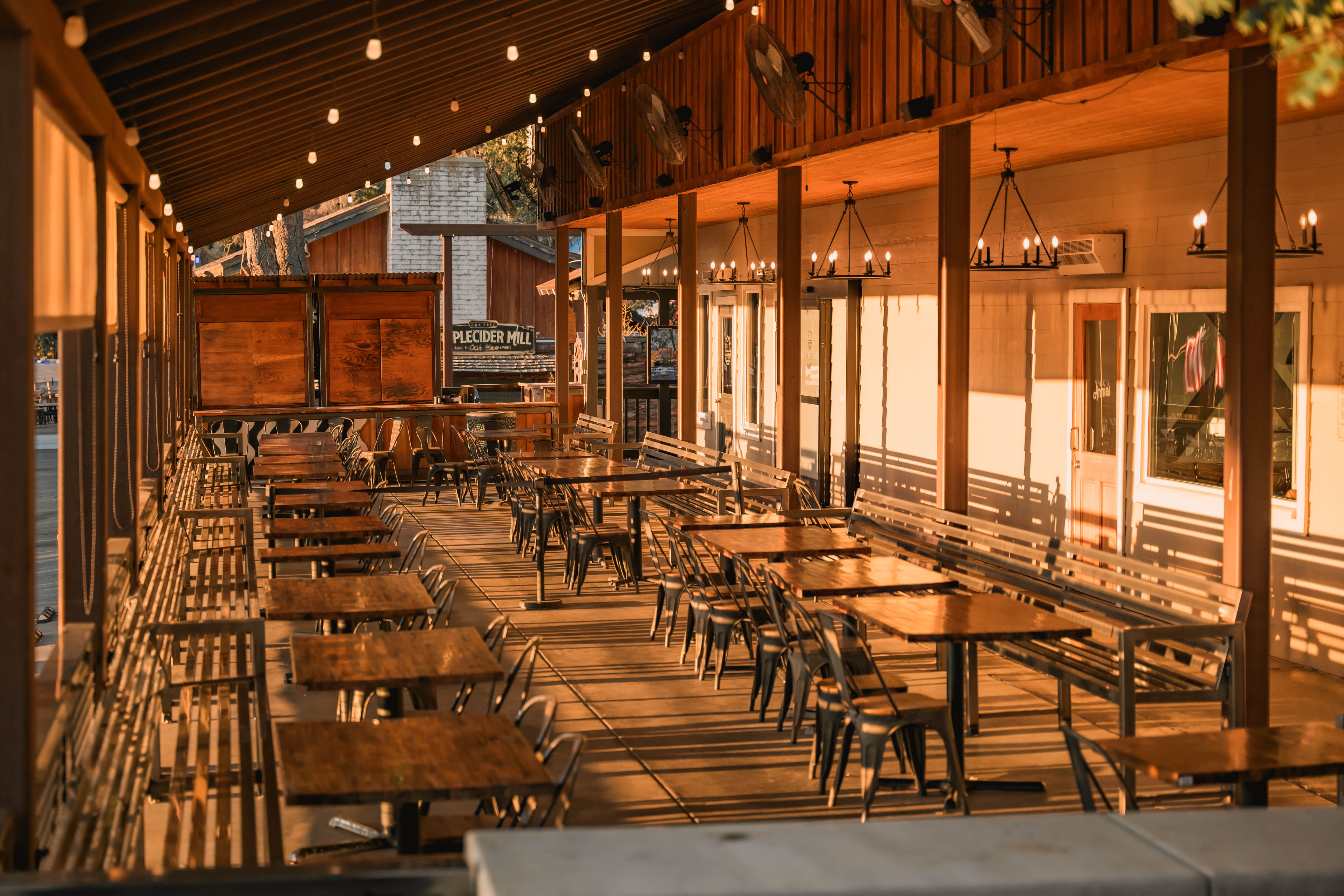 Warm outdoor patio with wooden tables, chairs, and ambient lighting for dining